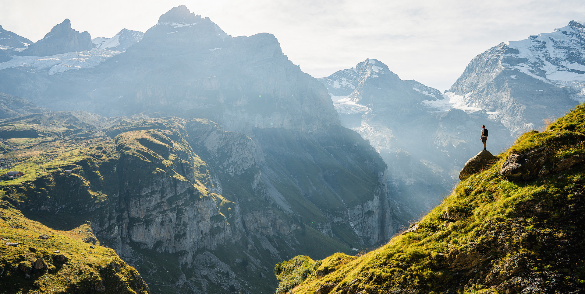 Wanderer steht auf Felsvorsprung mit Blick auf ein imposantes Alpenpanorama bei Sonnenaufgang