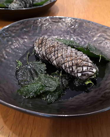 service3 Kreativ angerichtetes Gourmetgericht in Form eines Tannenzapfens mit Wildkräutern auf schwarzem Teller